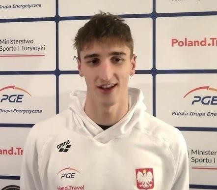 Ksawery Masiuk, polski pływak, w inspirującym portrecie zbliżeniowym, prezentujący skupioną i zdeterminowaną minę, w okularach pływackich i czepku, z delikatnymi kroplami wody na twarzy.