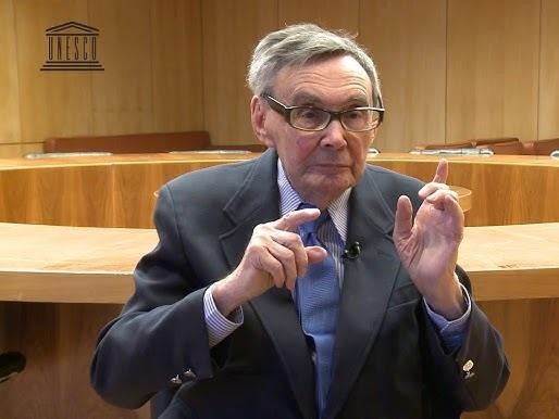 Marian Turski podczas przemówienia na tle upamiętniającym Holokaust, symbolizującego jego zaangażowanie w pamięć i edukację.