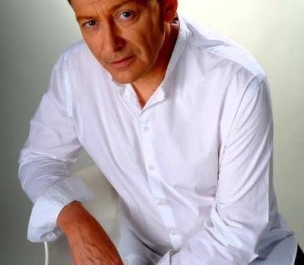 Jacek Borkowski na scenie, śpiewający lub grający, w dynamicznej pozie, oświetlony światłami scenicznymi.
