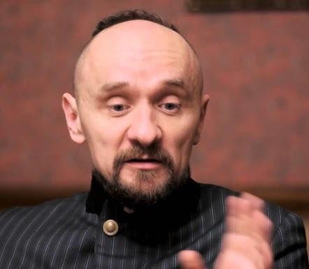 Dynamiczna scena teatralna w szerokim kadrze, ukazująca nowoczesną inscenizację w stylu Jana Klaty, z aktorami w ekspresyjnych pozach i nieszablonowym oświetleniem.