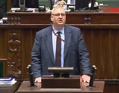 Bogdan Roman Święczkowski w dynamicznej pozie, symbolizującej jego bezkompromisowy styl zarządzania, z elementami nawiązującymi do wymiaru sprawiedliwości.