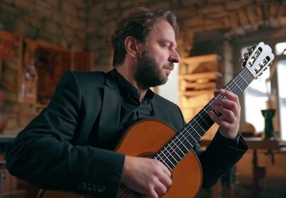 Marcin Dylla podczas występu na scenie, grający na gitarze klasycznej, w świetle reflektorów.