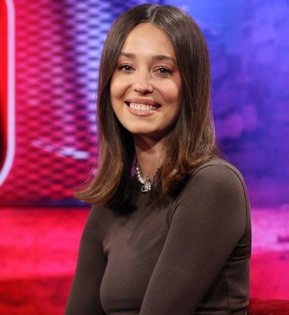 Izabella Krzan w spontanicznej chwili, śmiejąca się i pełna energii, w otoczeniu sugerującym plan telewizyjny lub wydarzenie medialne.