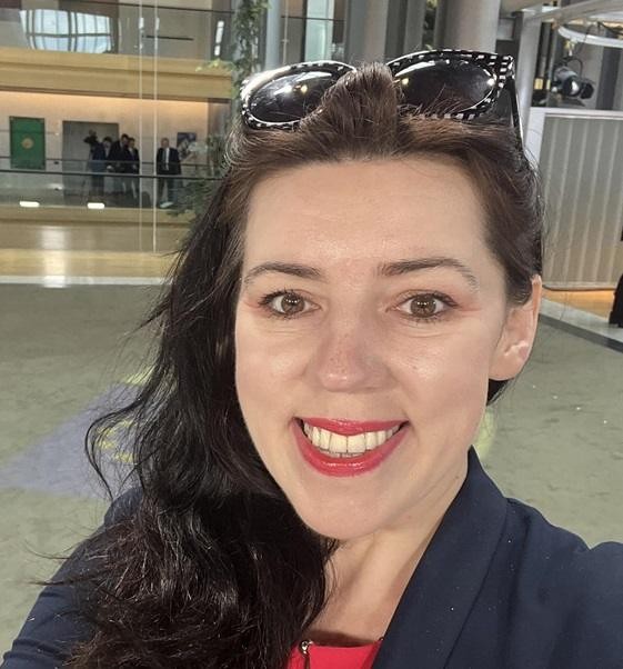 Dominika Ćosić w dynamicznej pozie, symbolizującej jej rolę dziennikarki i pisarki, na tle europejskiej instytucji lub bałkańskiego krajobrazu.