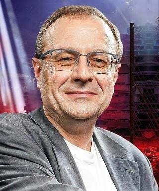 Antoni Dudek podczas wykładu lub prezentacji, dynamicznie gestykulujący, na tle tablicy z diagramami.