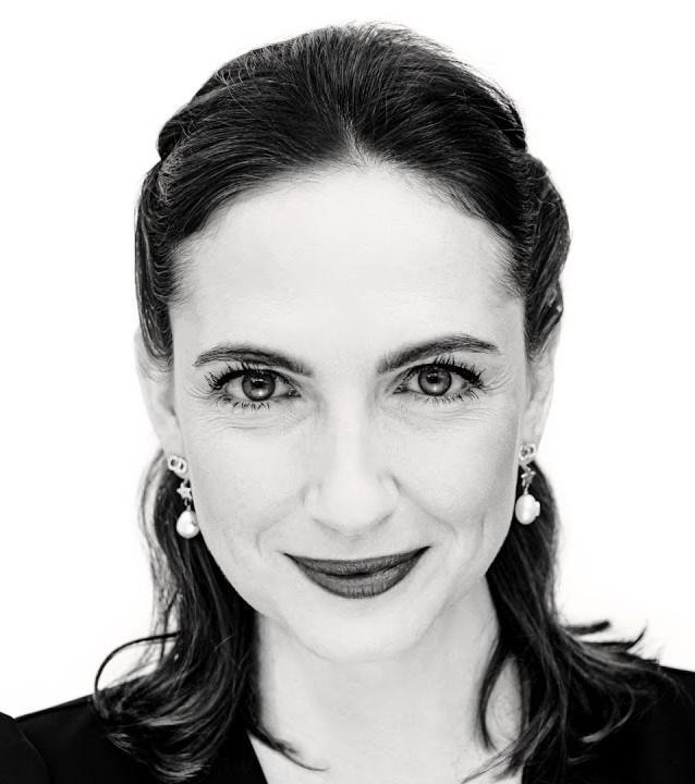 Anna Cieślak uśmiechająca się subtelnie w eleganckim, zamazanym wnętrzu.