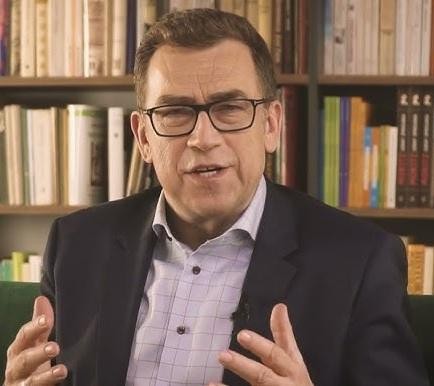 Maciej Orłoś podczas wystąpienia publicznego lub szkolenia, z ekspresyjną gestykulacją, podkreślającą jego rolę jako eksperta od komunikacji.