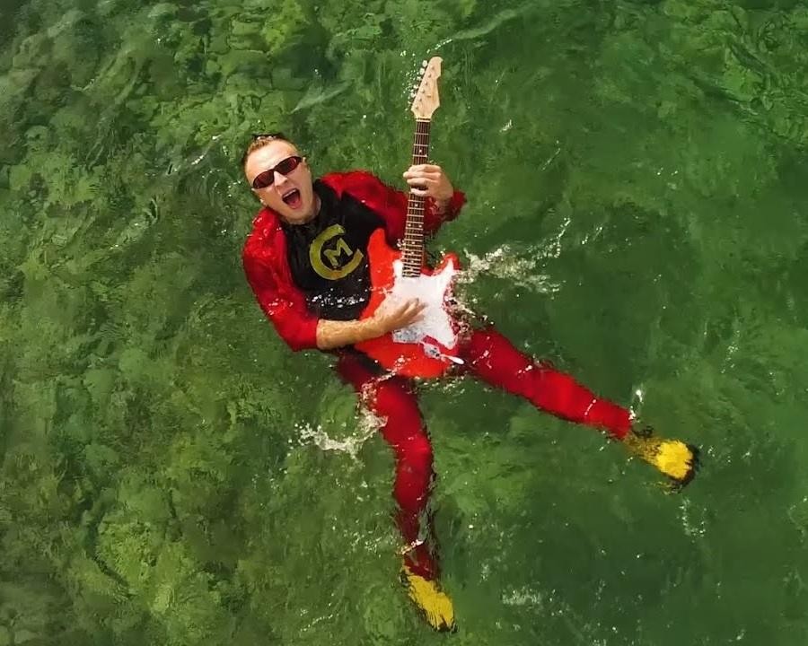 Czadoman (Paweł Dudek) podczas energicznego występu na scenie, śpiewający do mikrofonu, oświetlony kolorowymi światłami.